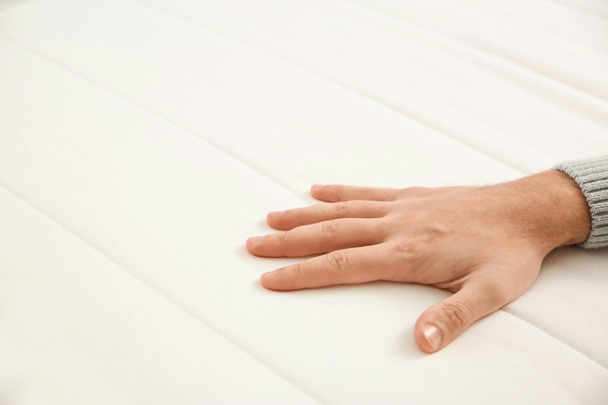 Man's hand pressing on a mattress to test its firmness level